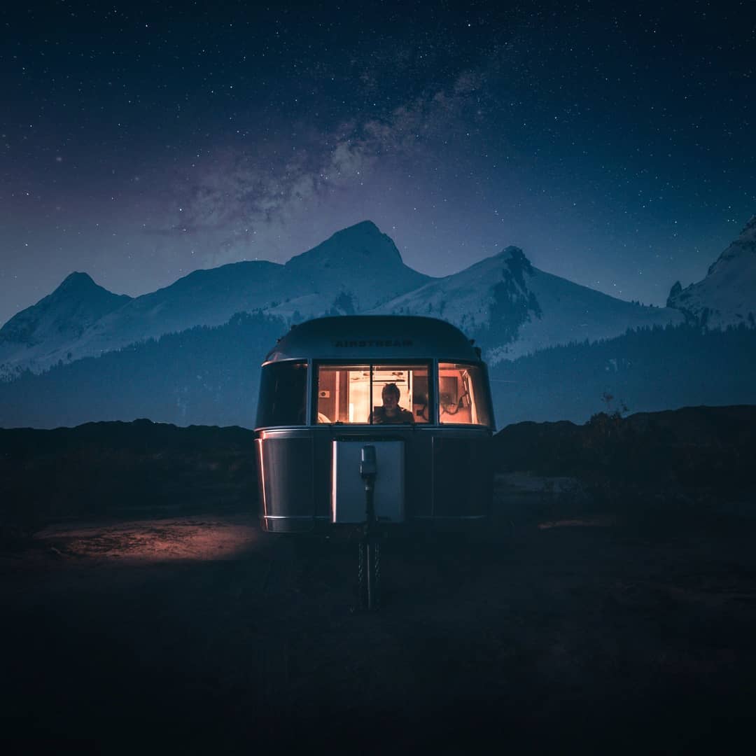 An Airstream lit from inside under the Milky Way